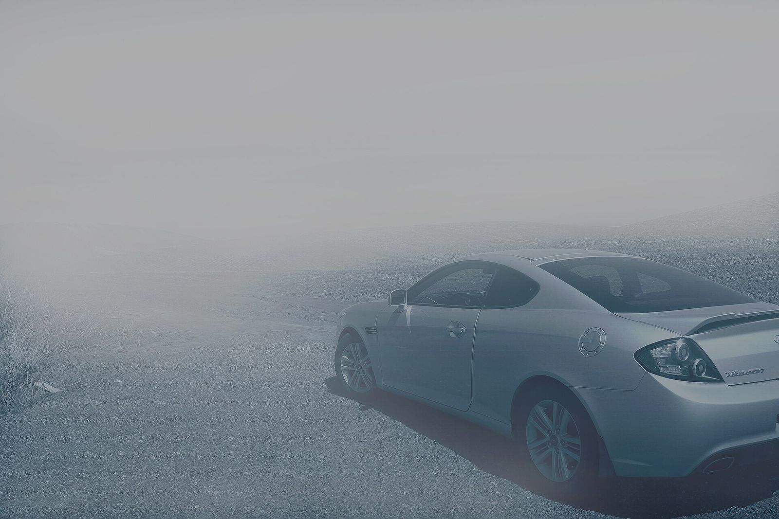 A silver coupe parked in fog